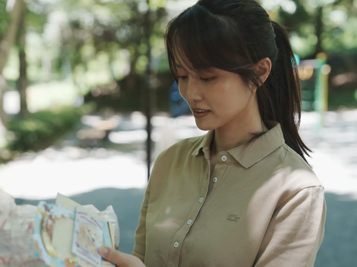 木漏れ日の公園で、ペットのメモリアルカードを開いて見つめる女性