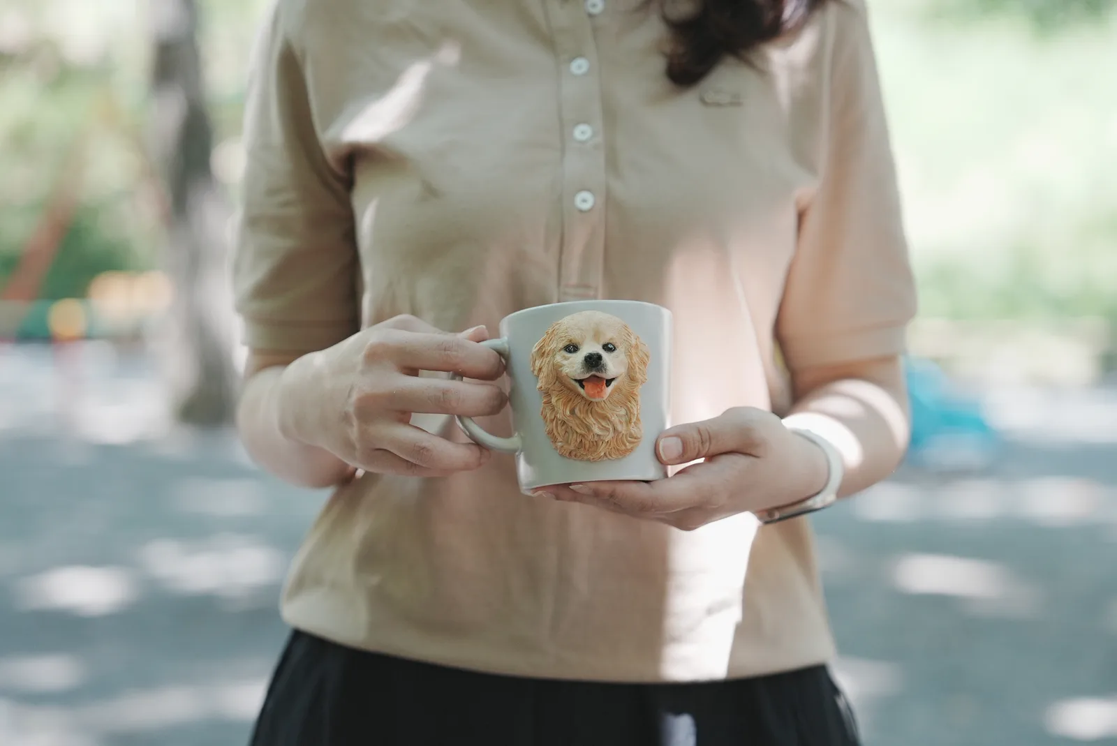 木漏れ日の下で、垂れ耳の犬の顔を立体にした白いマグカップを両手で持つ女性